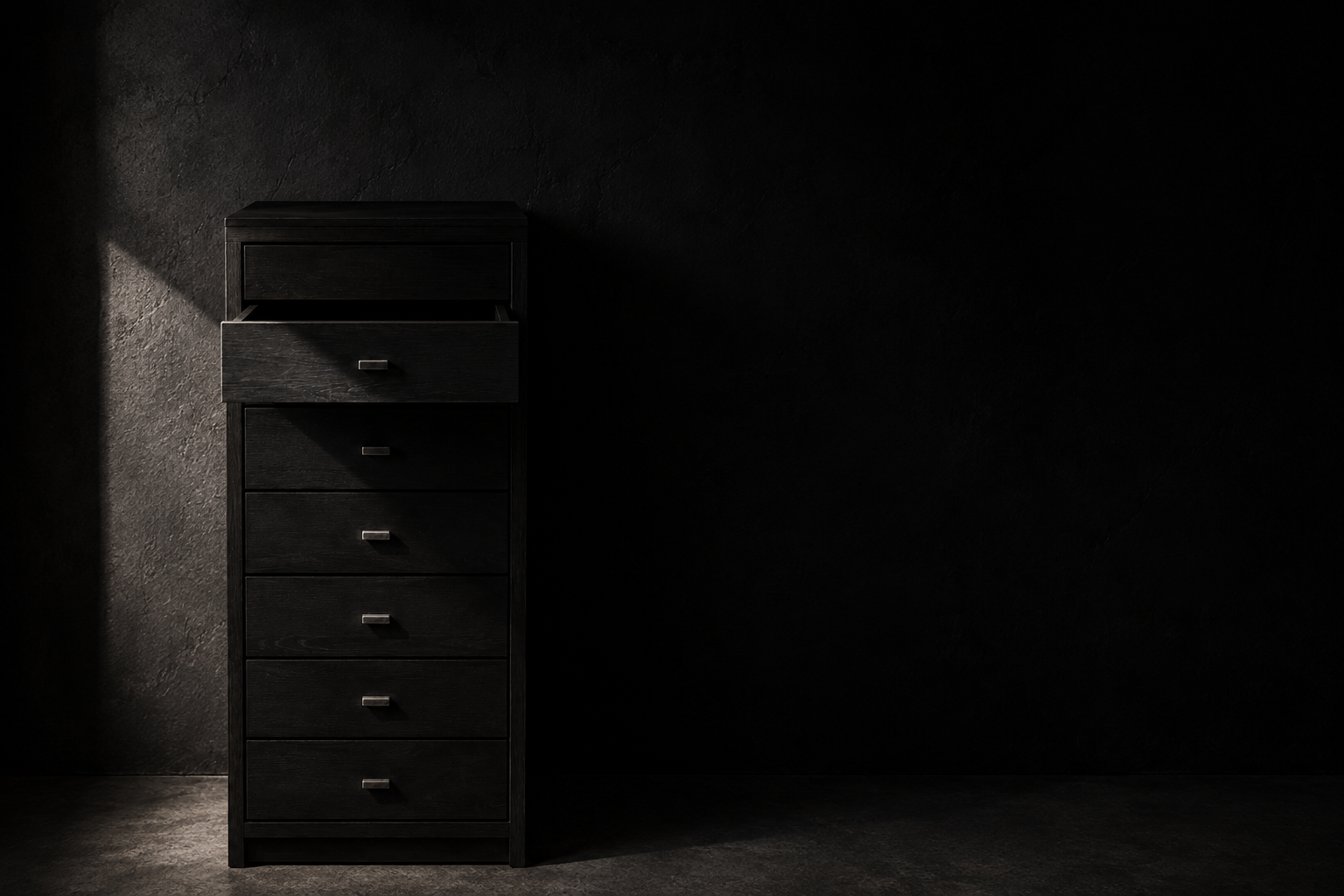 A dark wooden chest of drawers in a shadowed room with the top drawer pulled open